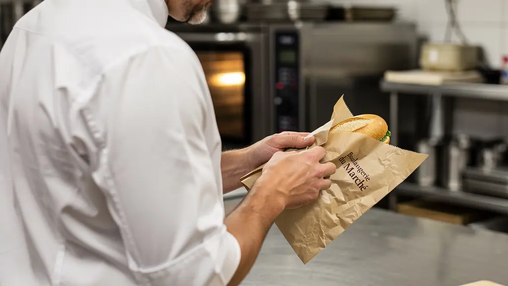 Cuisinier professionnel emballant un sandwich dans du papier personnalisé, vue par-dessus l'épaule en cuisine